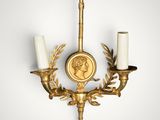 a gold plated wall sconce with two candles and a medallion