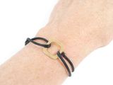 the hand is holding a black leather bracelet with a gold square on it