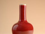 un vase rouge posé sur une table, sur fond beige