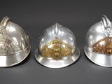 three silver and gold fire helmets sitting side by side on a gray surface