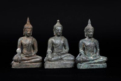 three bronze statues of buddhas sitting in a row on a black background