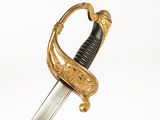 une épée ancienne ornée de motifs dorés et dotée d'une poignée noire sur fond blanc