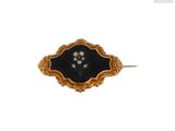 une photo d'une broche noire et dorée ornée de perles