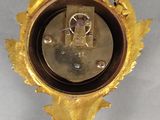 une horloge dorée accrochée au mur, sur un fond blanc