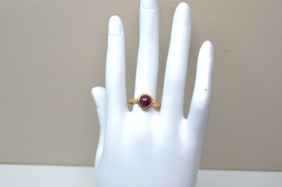 a hand with a ring on it that has a red stone on it