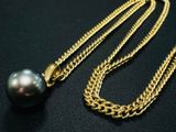 un collier composé d'une perle noire et d'une chaîne en or, posé sur une surface noire