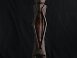 une sculpture en bois représentant une personne debout sur un fond noir