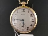 a gold pocket watch on a black surface with a price tag