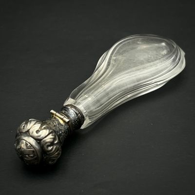 une cuillère en verre avec un manche en argent posée sur une surface noire