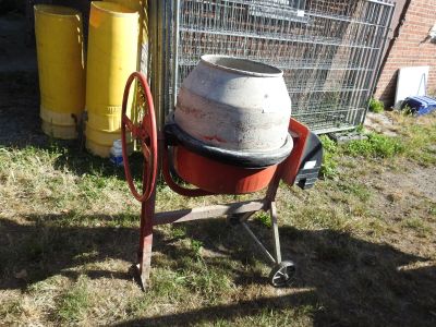 a cement mixer sitting in the grass next to a fence