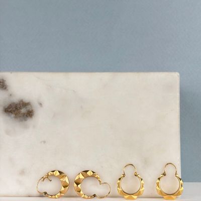 un lot de cinq boucles d'oreilles en anneau dorées posées sur une plaque de marbre
