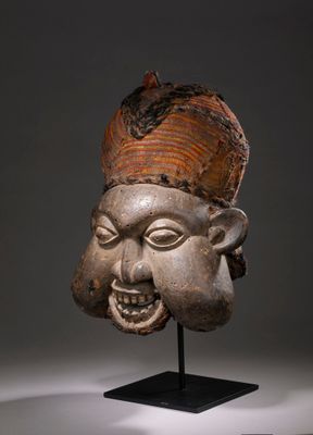 une image représentant un masque en bois posé sur un socle, sur fond gris