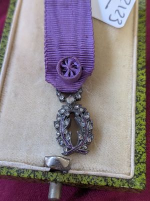 un ruban violet muni d'un fermoir argenté, posé sur un livre sur lequel est apposée une étiquette avec un nom