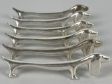 six teckels en métal plaqué argent sont alignés sur une surface blanche