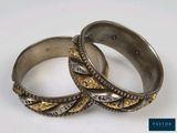 pair of silver and gold bangles on a white surface with a blue background