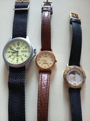trois montres sont alignées sur une surface blanche, avec un bracelet noir