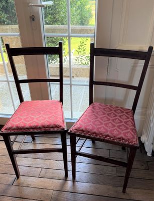 Deux chaises en bois, avec des coussins rembourrés roses, sont placées devant une fenêtre.