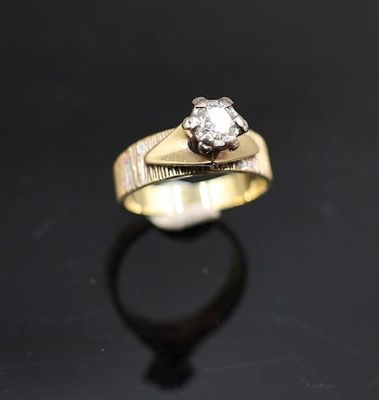 une bague en or sertie d'un diamant, posée sur un fond noir