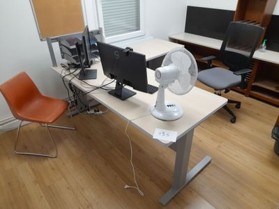 a desk with two computers and a fan on it