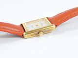 an orange watch with a gold case and a square face