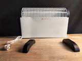 un radiateur électrique blanc posé sur une table, à côté de deux télécommandes