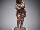 une statue en bronze représentant un garçon debout au sommet d'un bloc de marbre