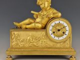 figurine en or représentant un garçon assis sur une horloge, en train de lire un livre