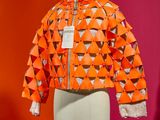 an orange jacket on a mannequin stand in front of a red wall