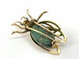 an image of a gold and green beetle broochle on a white background