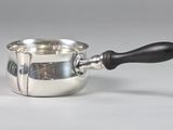 une saucière en argent avec une poignée noire posée sur une table blanche