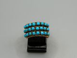 un gros plan d'une bague en or et turquoise posée sur un socle noir