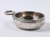 une vieille coupe en argent munie d'une anse, posée sur une surface blanche