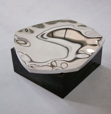 une assiette en argent posée sur un socle noir, sur une surface blanche