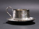 a silver cup and saucer sitting on a plate