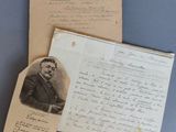 une vieille photo d'un homme en costume-cravate, assis à côté d'une feuille de papier sur laquelle sont inscrits des mots