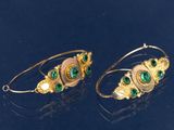 deux paires de boucles d'oreilles en or et émeraude posées sur un fond noir