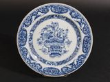 une vieille assiette bleue et blanche sur laquelle est représenté un panier de fleurs