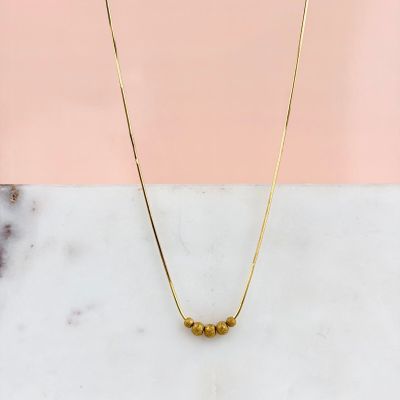 un collier en or orné de trois perles, posé sur une surface en marbre