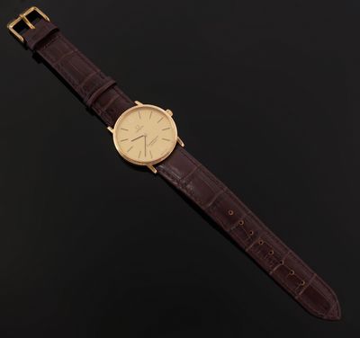 a gold watch with a brown leather strap on a black background