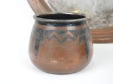 a small copper pot sitting next to a silver plate