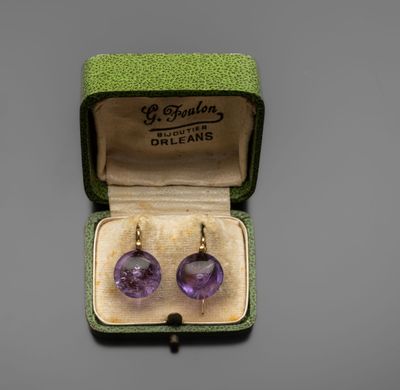 une photo d'une paire de boucles d'oreilles en verre violet dans une boîte verte
