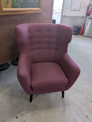 une chaise violette placée dans une pièce où est accroché un tableau au mur