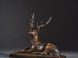 une sculpture en bronze représentant un cerf posé sur un socle en bois
