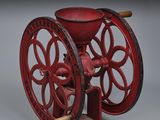 un vieux moulin à café rouge avec un manche en bois posé sur une surface grise