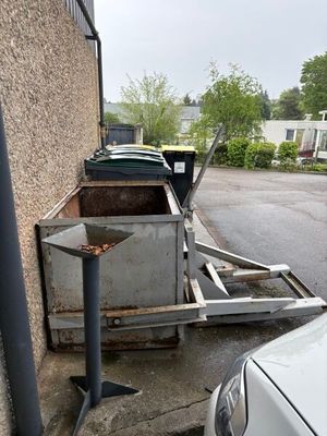 des voitures garées sur un parking à côté d'un immeuble où s'entasse un tas de vieilleries