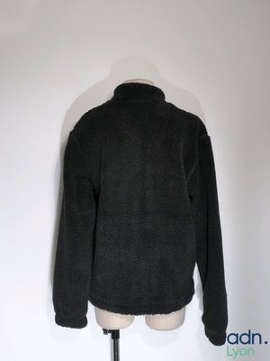 une veste noire posée sur un mannequin, devant un mur blanc