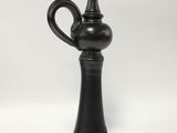 a black vase sitting on top of a table next to a white wall