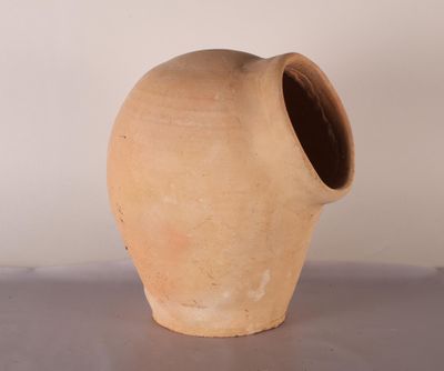 un vase en argile posé sur une table, avec un mur blanc en arrière-plan