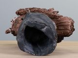 a black vase sitting on top of a table next to a piece of wood