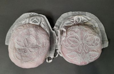 une paire de genouillères roses ornées de dentelle blanche, posées sur une table